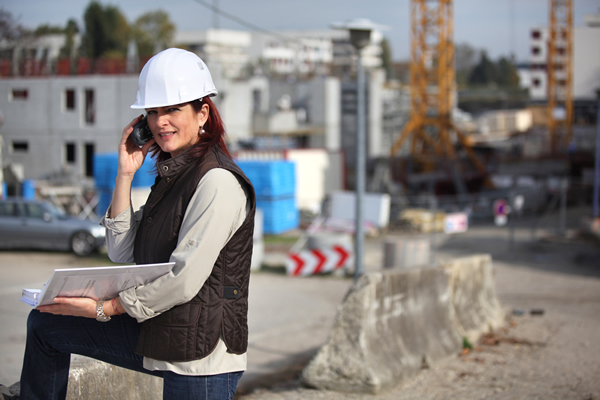 Gerente de proyectos arrodillado, con una carpeta y un teléfono celular, en un sitio de trabajo.