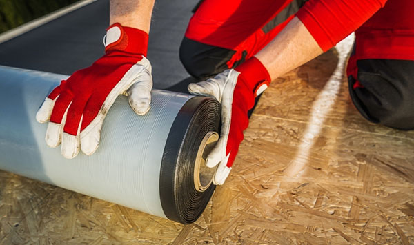 Un contratista de techado prepara un rollo de material de membrana para techos de EPDM.