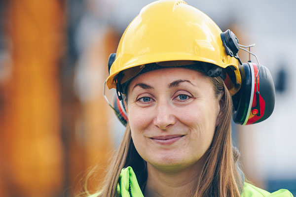 Mujer techadora sonriente con casco y auriculares de seguridad