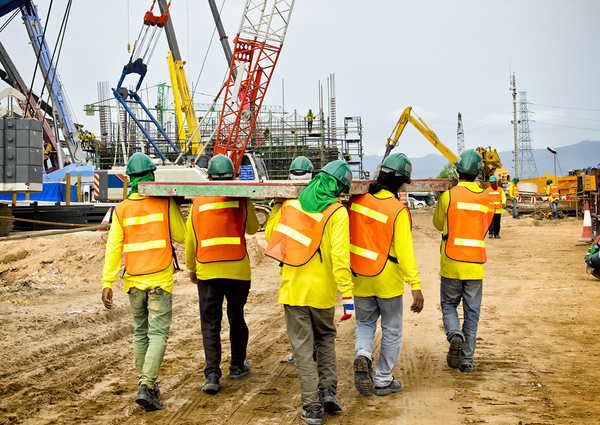 Una cuadrilla de construcción que camina por un sitio de trabajo con grúas de fondo