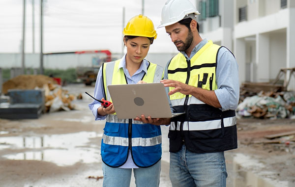 Dos personas que miran una computadora en una obra de construcción.