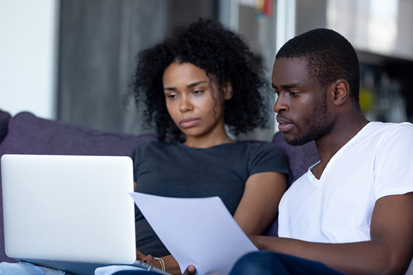 Una pareja joven (hombre y mujer) revisa información en una computadora portátil y examina documentos.