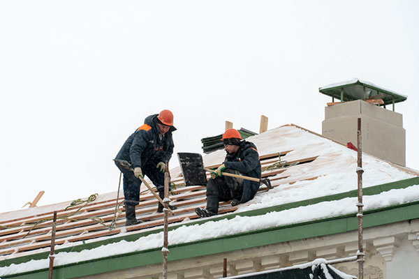 Dos techadores con equipos de seguridad sobre un techo cubierto de nieve.