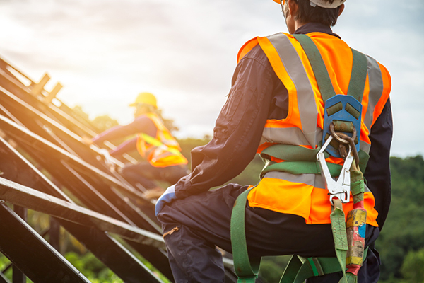 Dos trabajadores de la construcción con arneses de seguridad trabajando en la estructura de un techo