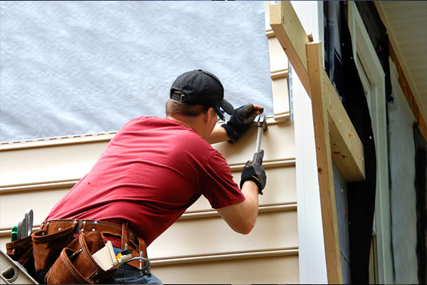 A man installs beige-colored siding on the side of a home.