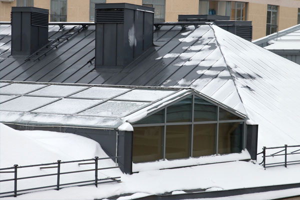 Techo con juntas de plegado saliente con una pendiente pronunciada sobre un edificio cubierto de nieve.