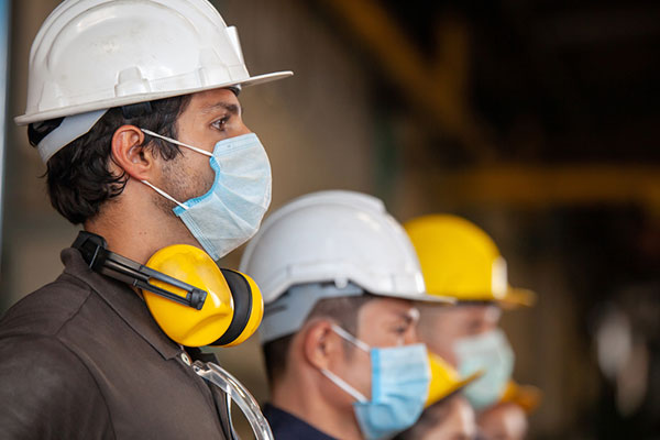 Trabajadores de la construcción con máscaras, cascos y protección para los oídos esperan en fila para recibir instrucciones